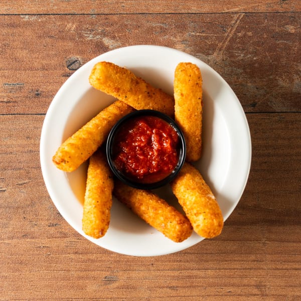 Crispy golden mozzarella sticks with a side of marinara sauce in a white bowl on a wooden surface.