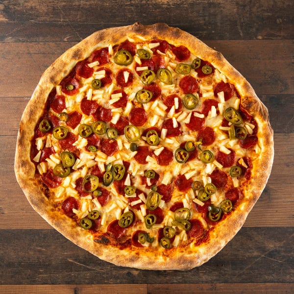 Whole pepperoni, pineapple, and jalapeño pizza on a dark wooden surface.