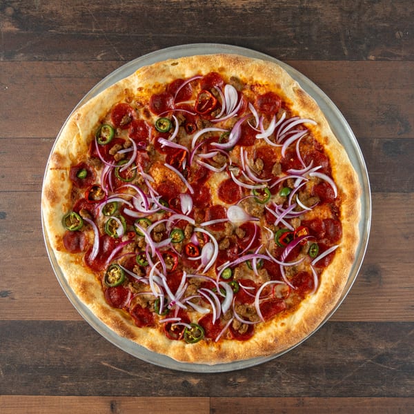 Whole pizza with pepperoni, sausage, red onions, and jalapeños on a wooden table.