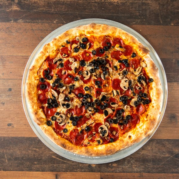 Pepperoni, mushroom, and black olive pizza on a metal tray over a wooden table.
