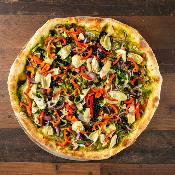 Vibrant pesto pizza with red and green peppers, black olives, red onions, and artichoke hearts.