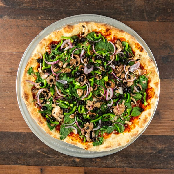 A large vegetarian pizza with spinach, green peppers, mushrooms, olives, and red onions on a wooden table.