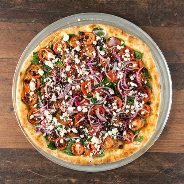 Gourmet pizza with tomatoes, red onions, black olives, feta cheese, and spinach on a metal tray.